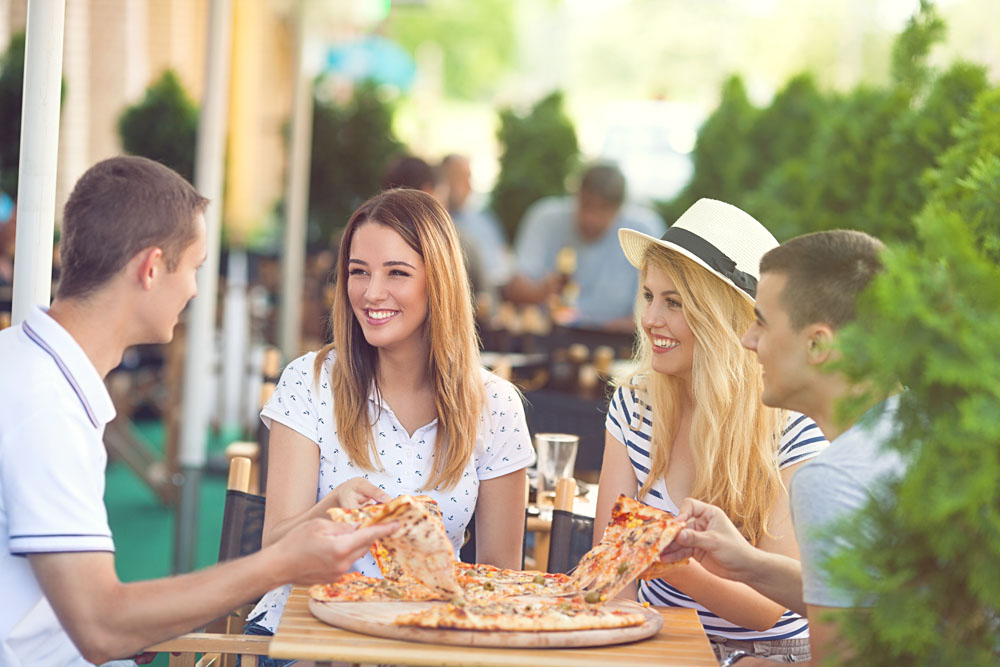 Four Cheerful Young Friends Sharing Pizza in an Outdoor Cafe