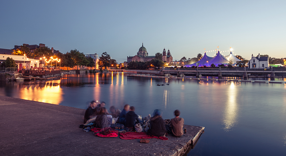Enjoying the evening during Galway Art Festival with Big Top and Cathedral on the bank of Corrib river in Galway, Ireland