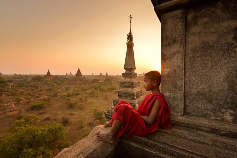 Novice young monk looking out at plains of Bagan during sunrise, Myanmar