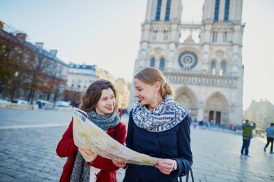 Two young girls walking together with map near Notre-Dame Cathedral, Paris, France