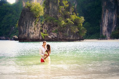 Couple stand in sea water in island bay with karst in background, Thailand