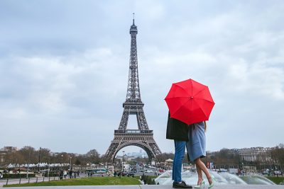 Honeymoon in Paris, Couple kissing behind red umbrella against Eiffel Tower, France