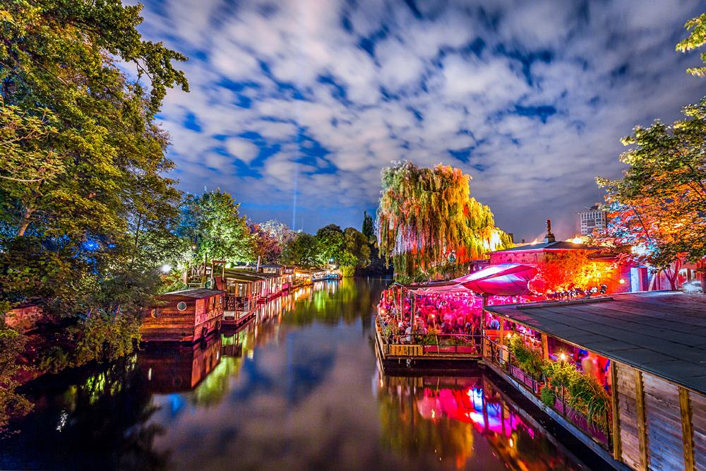 Panoramic view of young people partying in an open-air outdoor club at famous Flutgraben Water Canal, Berlin, Germany