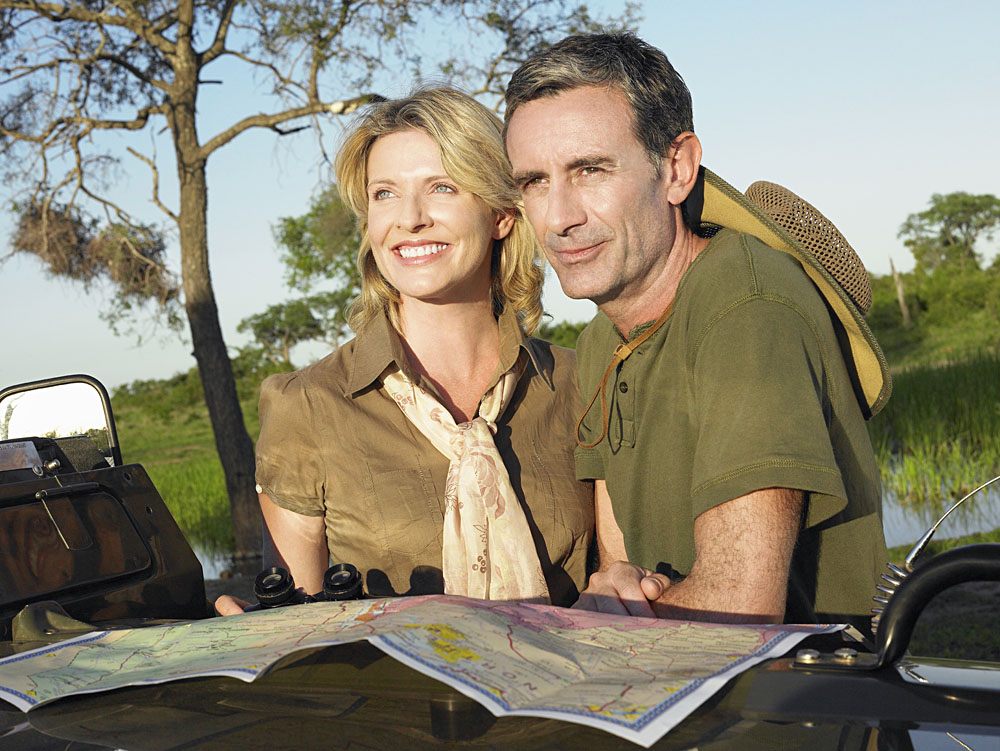 Smiling couple with at map on bonnet of jeep looking at view, Africa safari