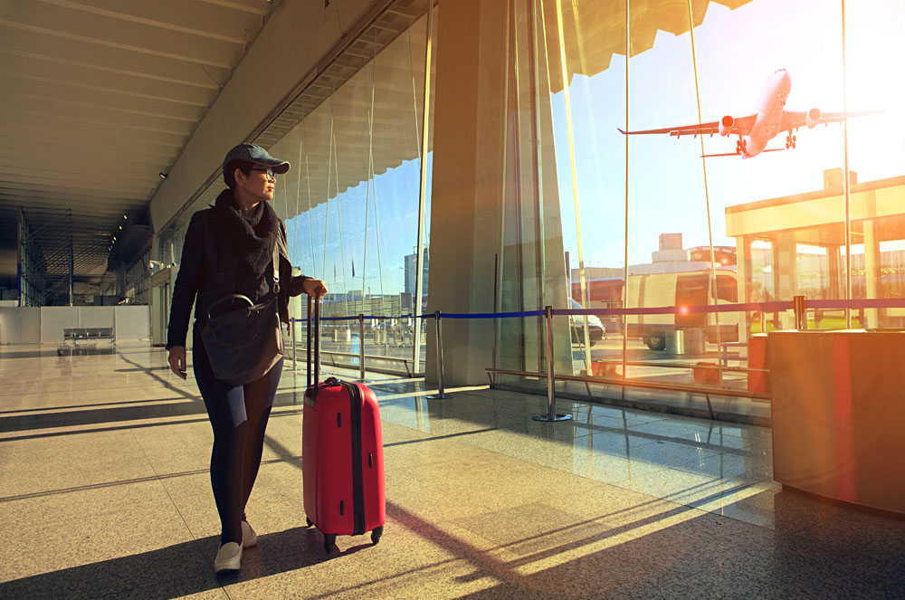 Traveling woman and luggage walking in airport terminal and airplane flying outside