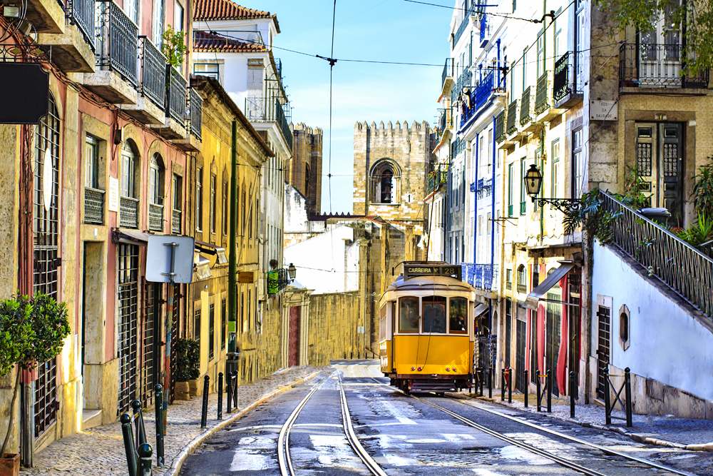 Romantic Lisbon street with the typical yellow tram and Lisbon Cathedral in the background, Portugal