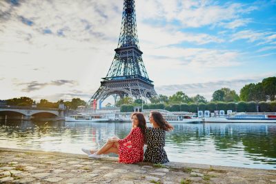 Twin sisters in red and black polka dot dresses in front of the Eiffel tower near the River Seine in Paris, France