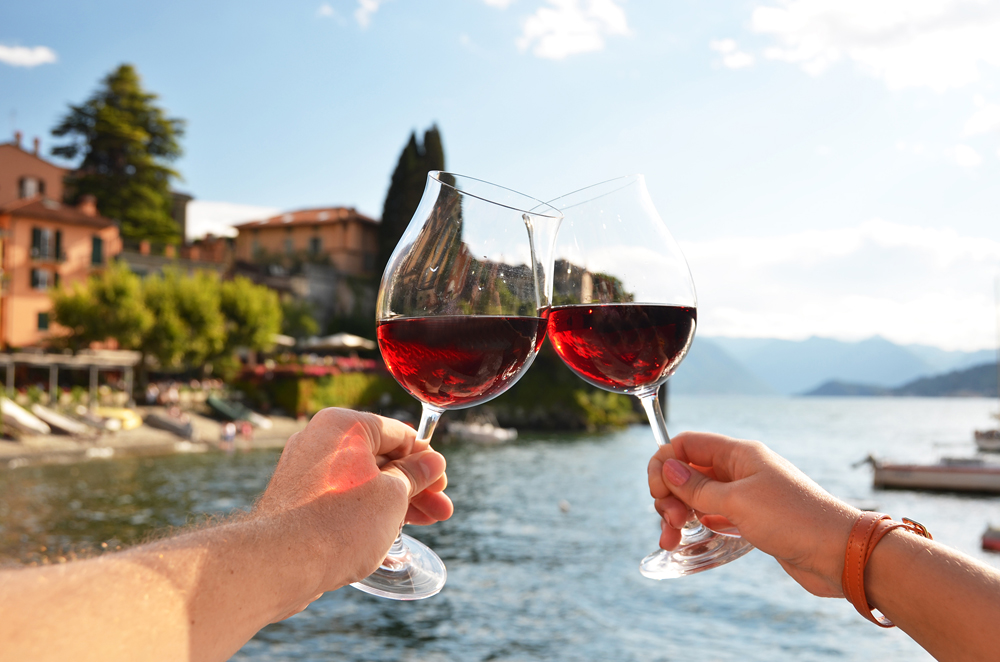 Two wineglasses clinking in Varenna town at Lake Como, Lombardy, Italy