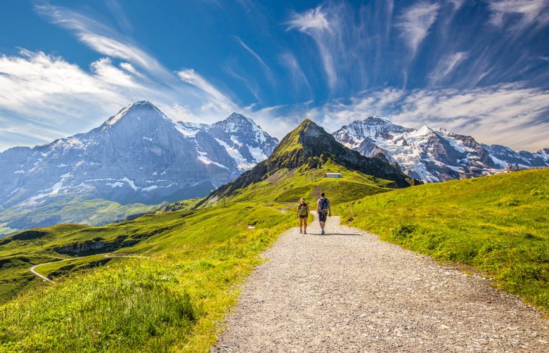 Young couple hiking in trail leading to Kleine Scheidegg from Mannlichen with Swiss Alps in the background, Switzerland