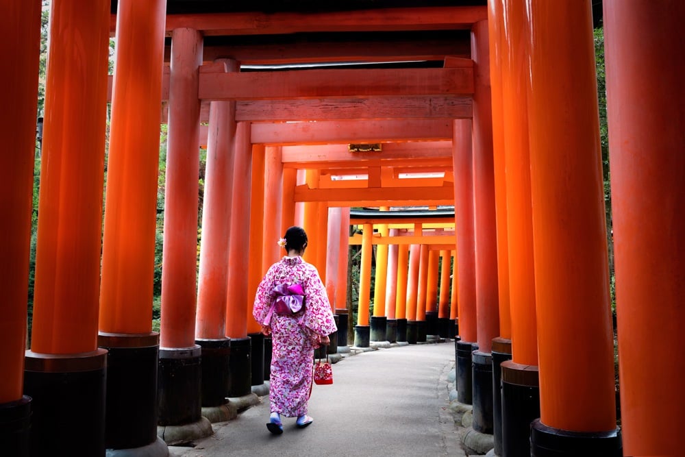 Traditionally dressed woman walking under Tori Gates at the Fushimi-inari Shrine, Kyoto, Japan 