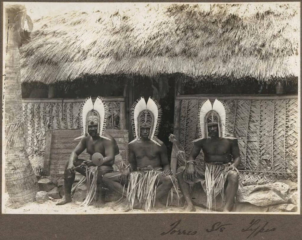 Frank Hurley - Torres Straits Types (three men wearing head dresses sitting outside hut), Torres Strait Islands, circa 1921
