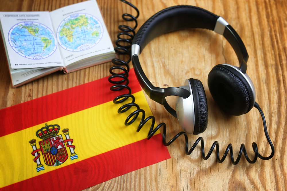 Spanish language course headphone and flag on wooden table 