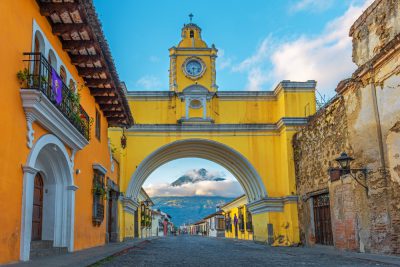 Colourful yellow arch of Guatemala Antigua city at sunrise with the active Agua volcano in the background, Guatemala