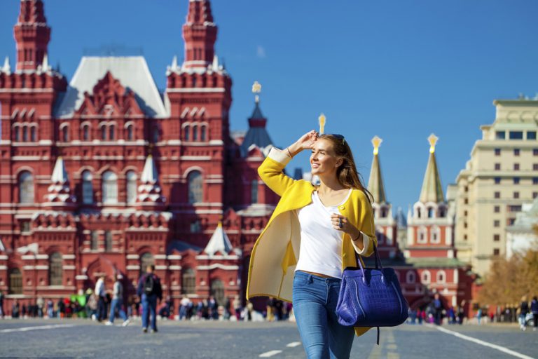 Young happy woman in yellow coat walking in Red Square in Moscow, Russia