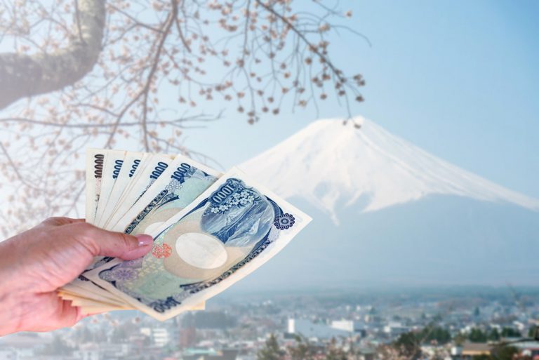 Hand holding Japanese Yen, isolated on blurred Fuji mountain in Japan