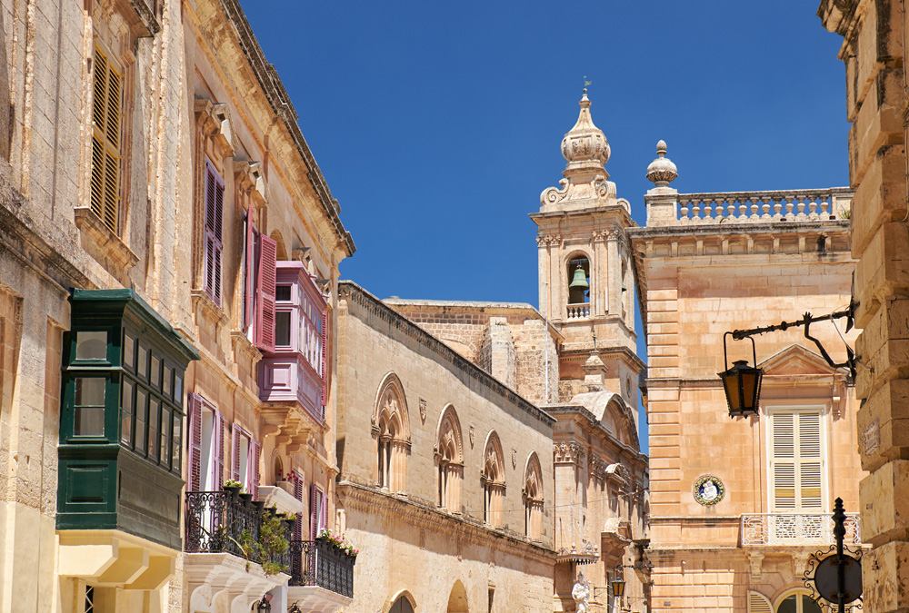 Old Mdina street with traditional Maltese style houses and Carmelite Church Bell Tower in the background, Mdina, Malta 