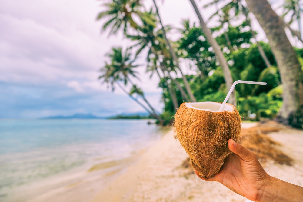 Woman holding fresh coconut water drink on beach in Bora Bora, Tahiti (French Polynesia) 