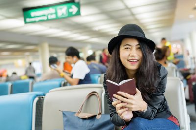 Young Asian woman solo traveller holding passport and waiting for flight travel at airport terminal