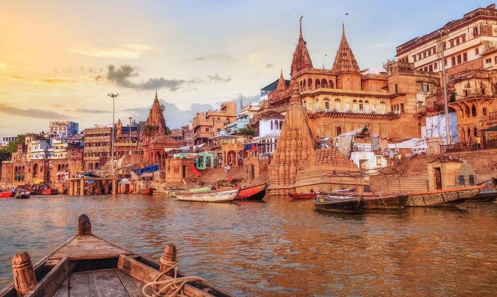 Ganges River ghat with ancient city architecture as viewed from a boat on the river at sunset, Varanasi, India 