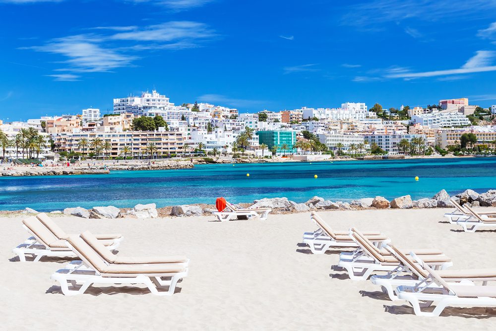 Sunbeds and city view on a beautiful beach in Ibiza, Balearic Islands, Spain 