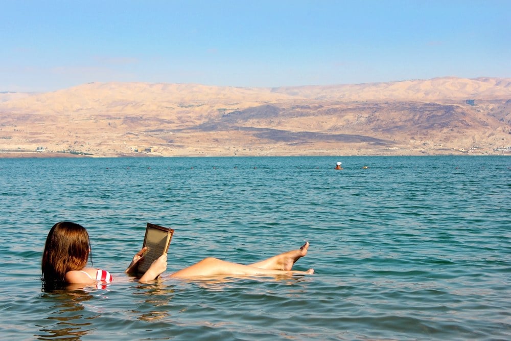 Young woman reads a book floating in the waters of the Dead Sea in Israel 