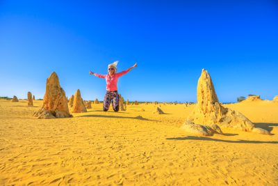 Blond girl jumping in the Pinnacles desert of Nambung National Park, Western Australia, Australia