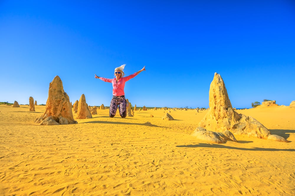 Blond girl jumping in the Pinnacles desert of Nambung National Park, Western Australia, Australia