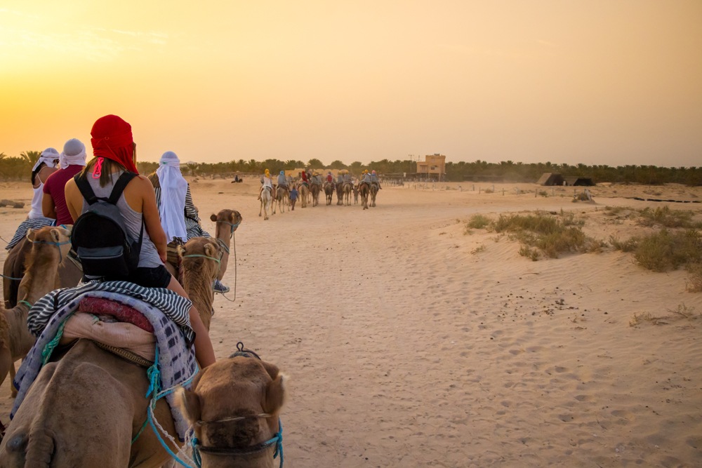 Tourists and Bedouins on camels at sunset in the Sahara desert, Douz, Tunisia 