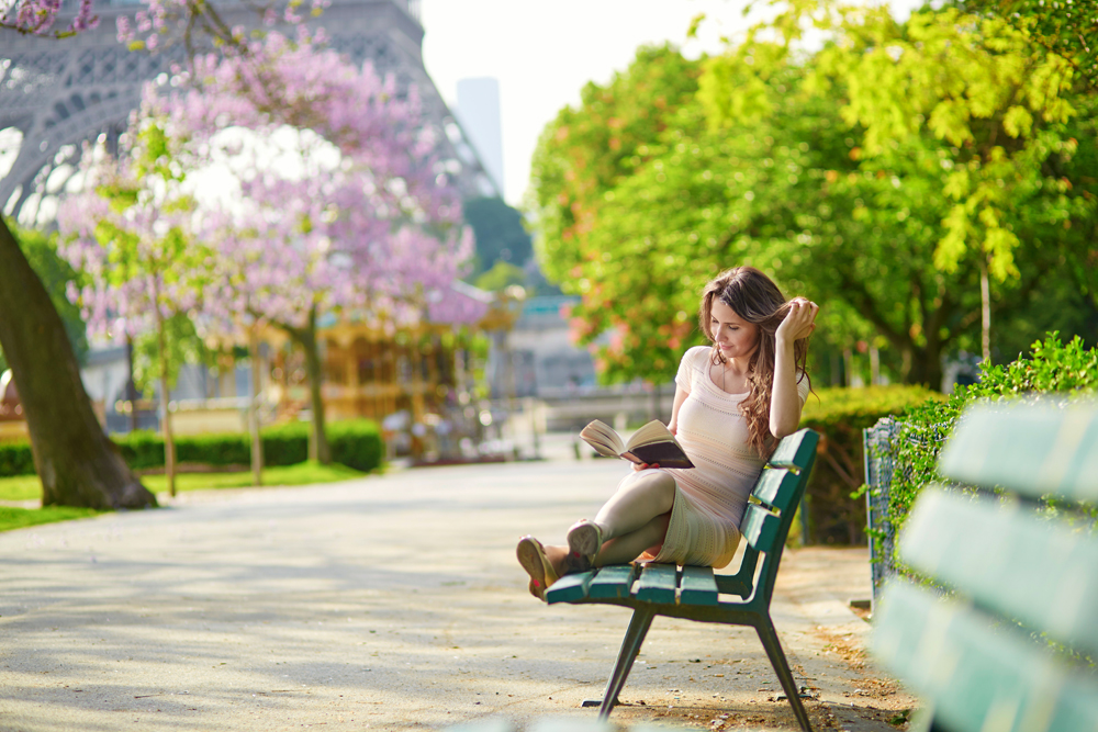 Young woman near the Eiffel Tower, reading on a bench, Paris, France