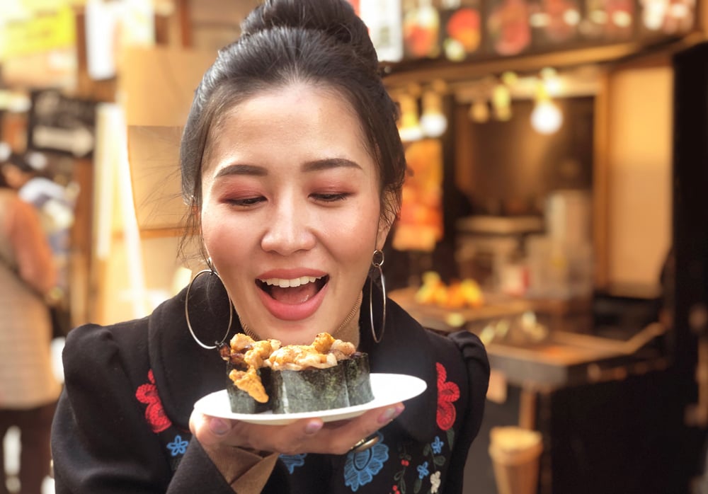 Woman with beef sushi at street food stall at Tsukiji Fish Market, Tokyo, Japan