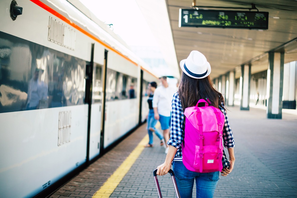 Female tourist with backpack and suitcase waiting for train on railway station 