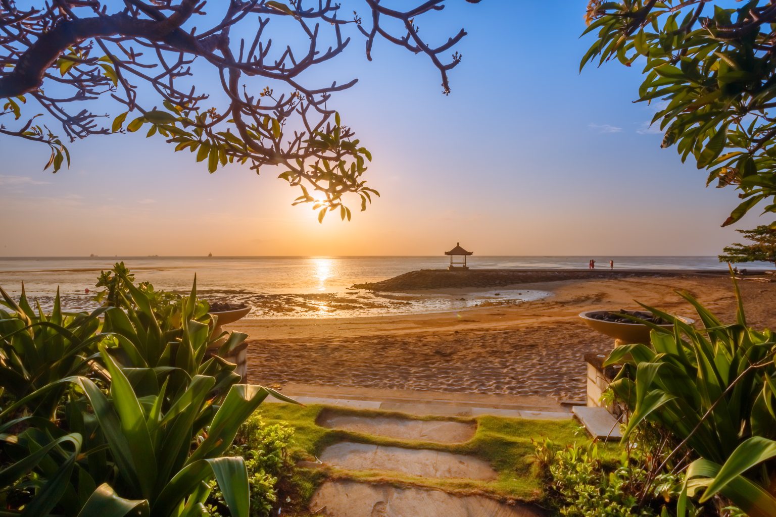  A view of the beach in Denpasar, Bali, Indonesia, with a sunset over the ocean.